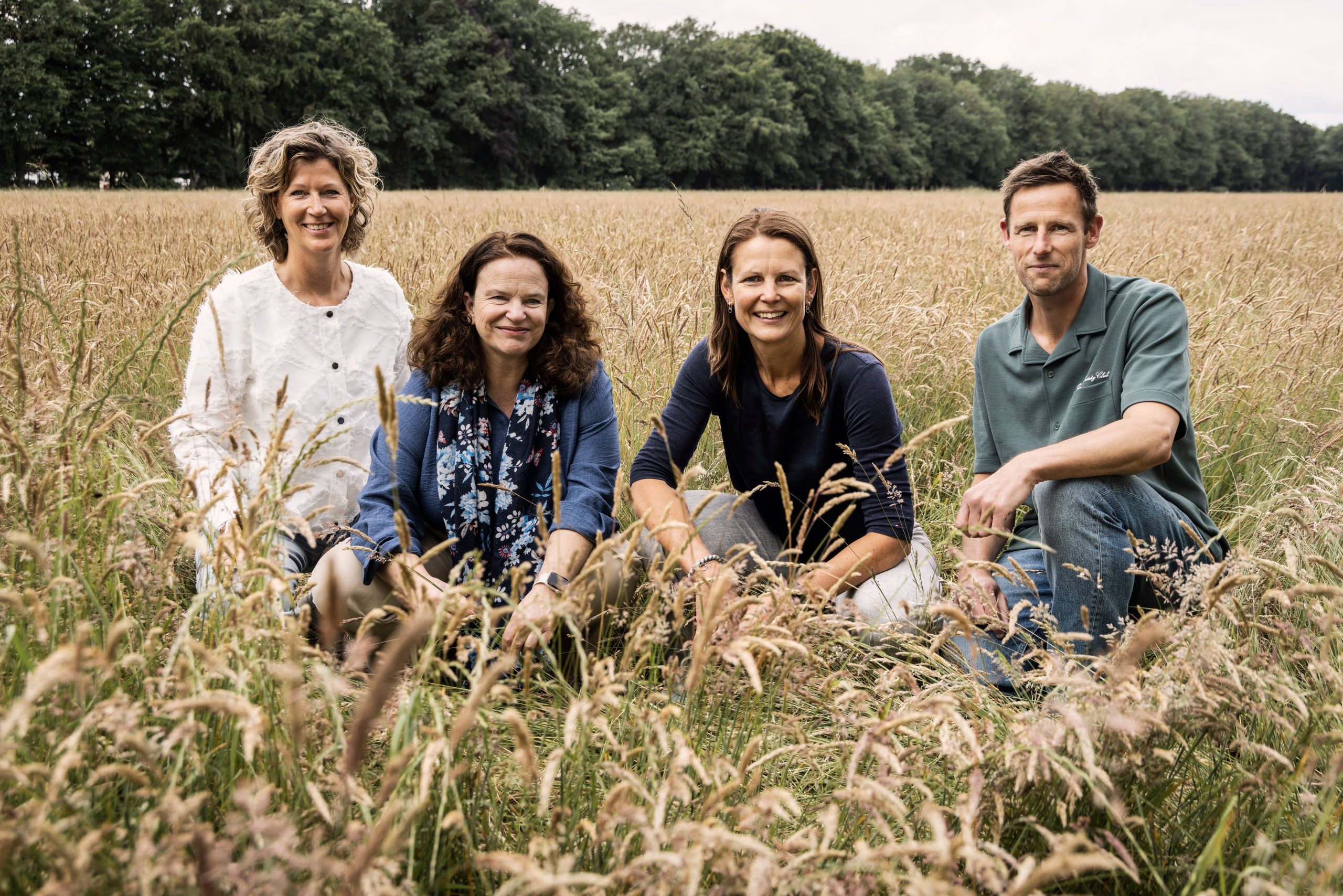 Een teamfoto van het Leitsager team. Ze zitten in het lange gras, gehurkt. We zitten bewust in het lange gras om te laten zien dat echte groei tijd en ruimte nodig heeft. Net als in de natuur, floreert verbetering het beste in een omgeving waarin er genoeg ruimte gegeven wordt.